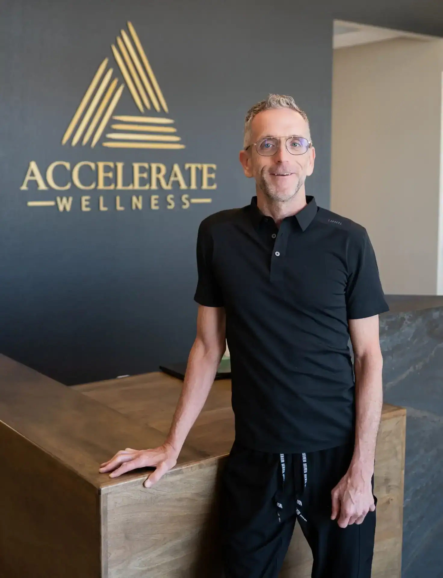 Rich Zieske, PA-C, smiling in a black collared shirt in front of the Accelerate Wellness logo wall.